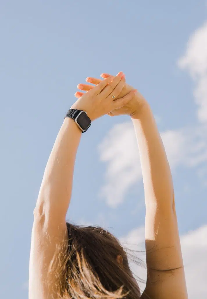 Personne s’étirant bras levés sous un ciel bleu, pour une activité physique douce et relaxante.