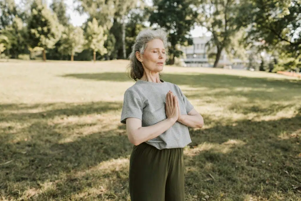 Femme âgée méditant debout dans un parc, calme et concentrée