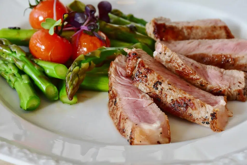 Tranches de viande grillée servies avec asperges vertes et tomates cerises, représentant un repas complet et adapté