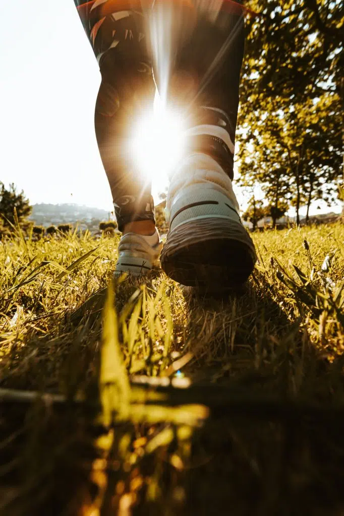 Personne marchant dans l’herbe au lever du soleil, illustrant un départ progressif vers une activité physique adaptée.