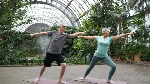 Deux personnes âgées pratiquent une séance de yoga dans un jardin couvert, pour illustrer l’importance du sport dans la gestion de la glycémie chez les diabétiques.