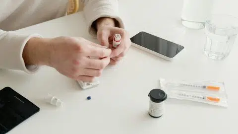 Personne effectuant une mesure de glycémie avec un autopiqueur, une bandelette et un lecteur de glycémie, sur une table à domicile.