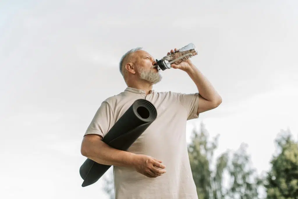 Homme senior tenant un tapis de sport et buvant de l’eau, illustrant la prévention active du prédiabète par l’activité physique et l’hydratation