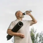 Homme senior tenant un tapis de sport et buvant de l’eau, illustrant la prévention active du prédiabète par l’activité physique et l’hydratation