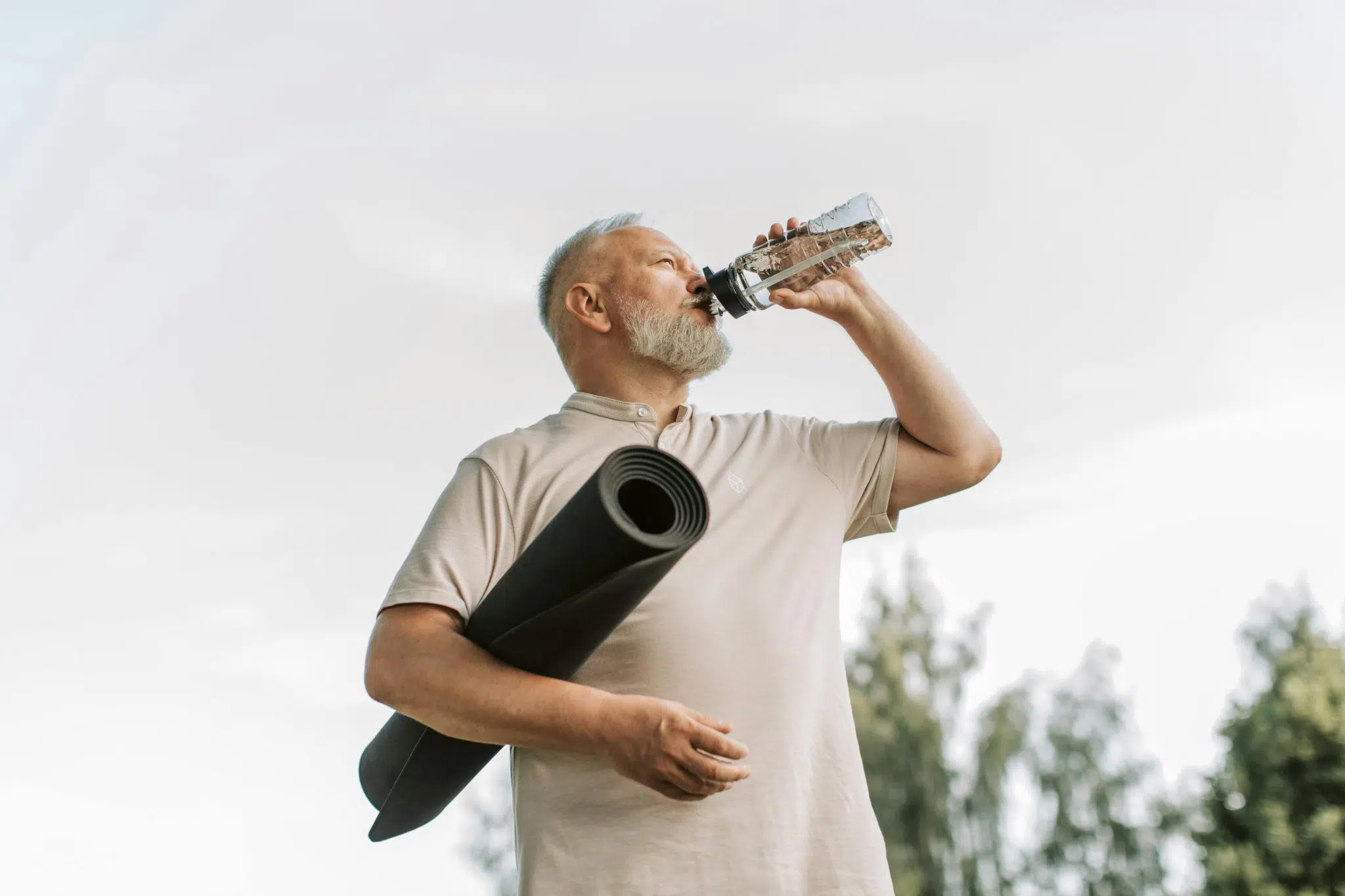 Homme senior tenant un tapis de sport et buvant de l’eau, illustrant la prévention active du prédiabète par l’activité physique et l’hydratation